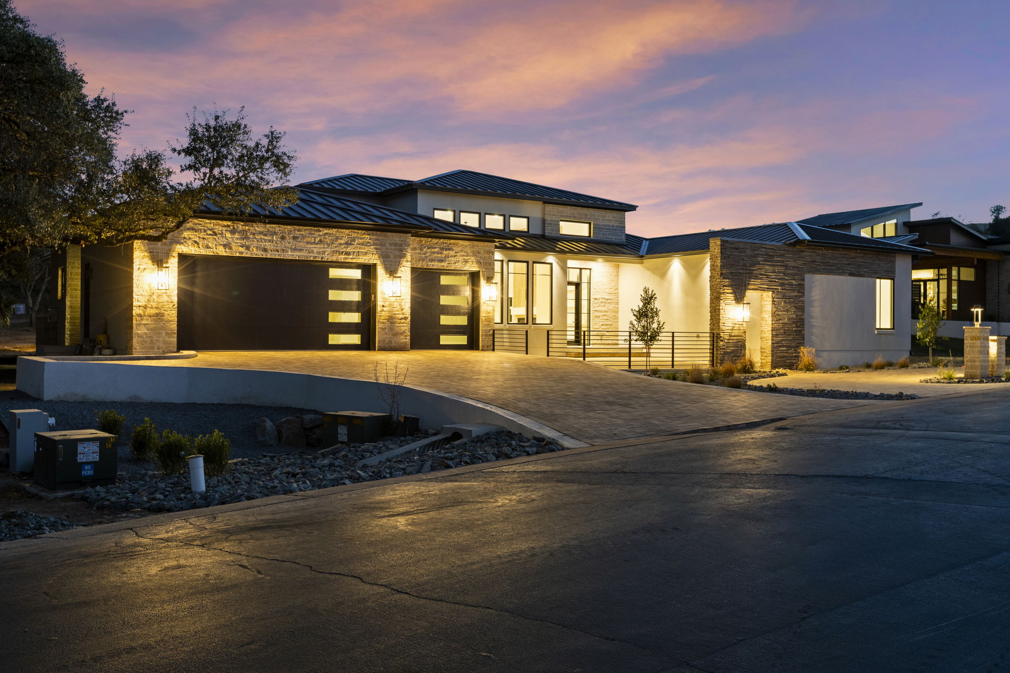Blue Hour, a custom home in Horseshoe Bay with limestone walls, dark metal roofs, and illuminated rooms at sunset