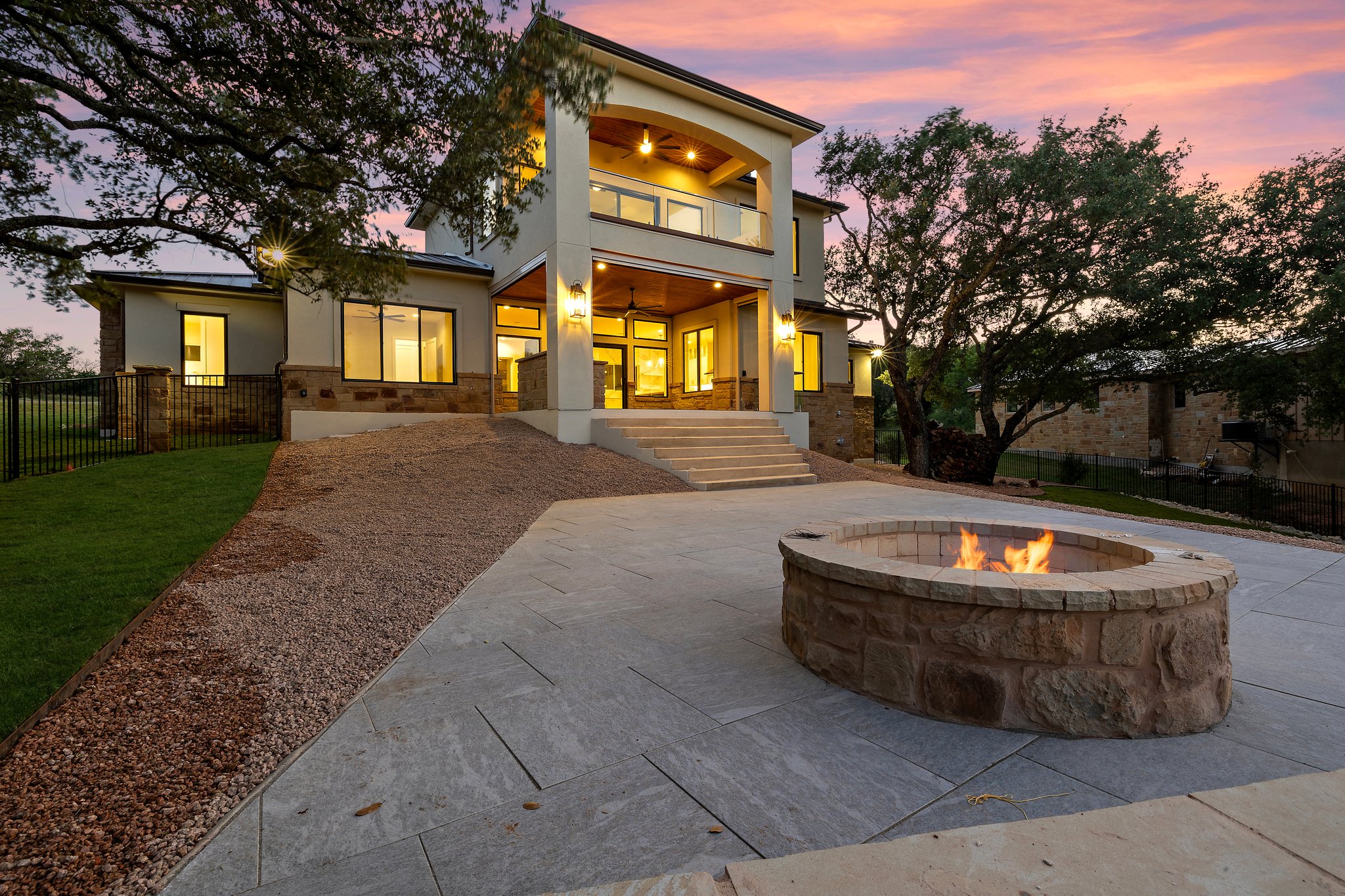 The Hideaway custom home with a covered terrace, mature oaks, and a stone fire pit in Horseshoe Bay